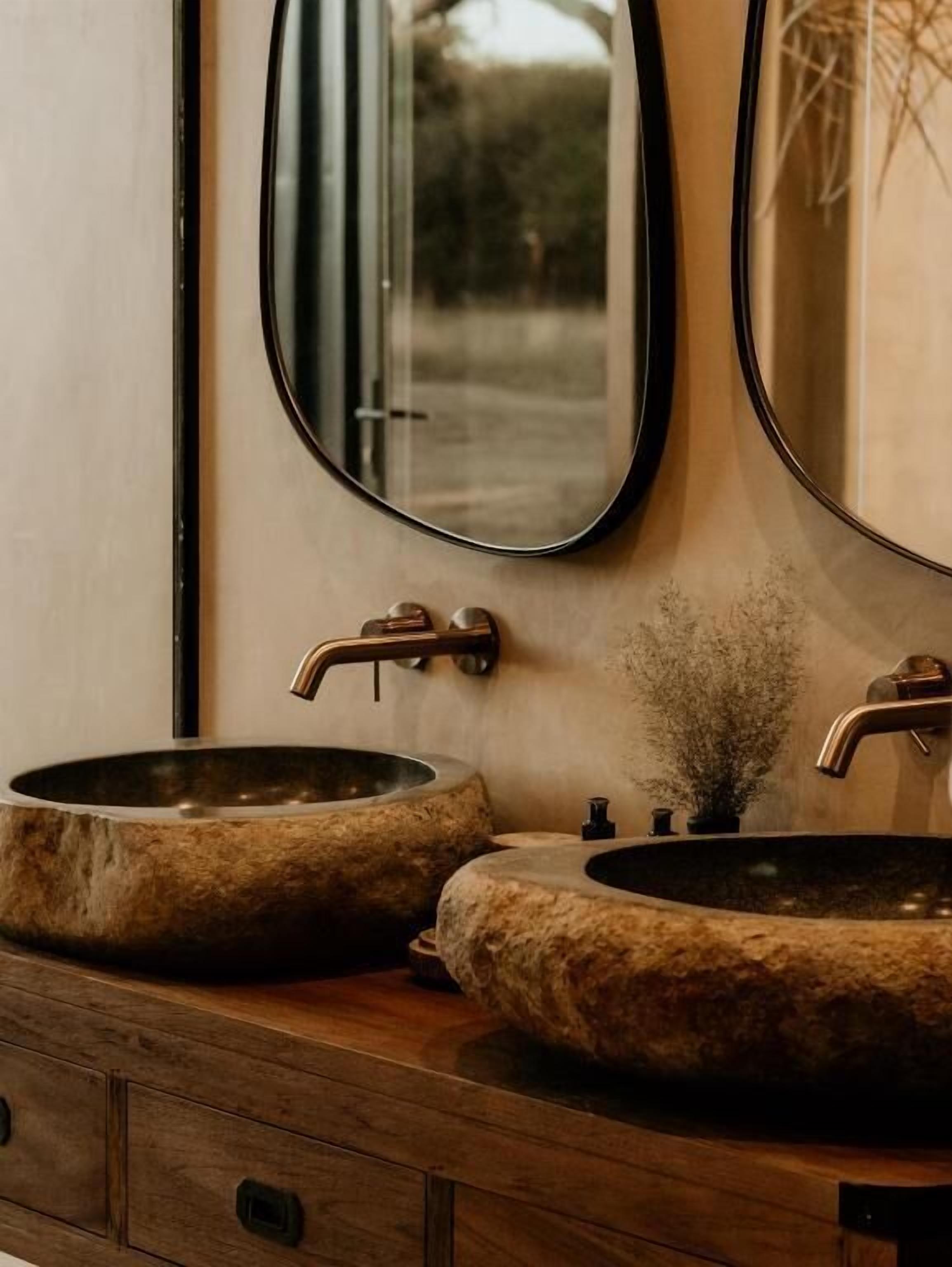 A bathroom with two round stone sinks, a wooden vanity, and a mirror.