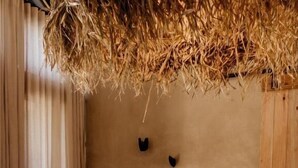 A room with a straw ceiling, a wooden bench, a sofa, and a wall-mounted shelf with decorative items.