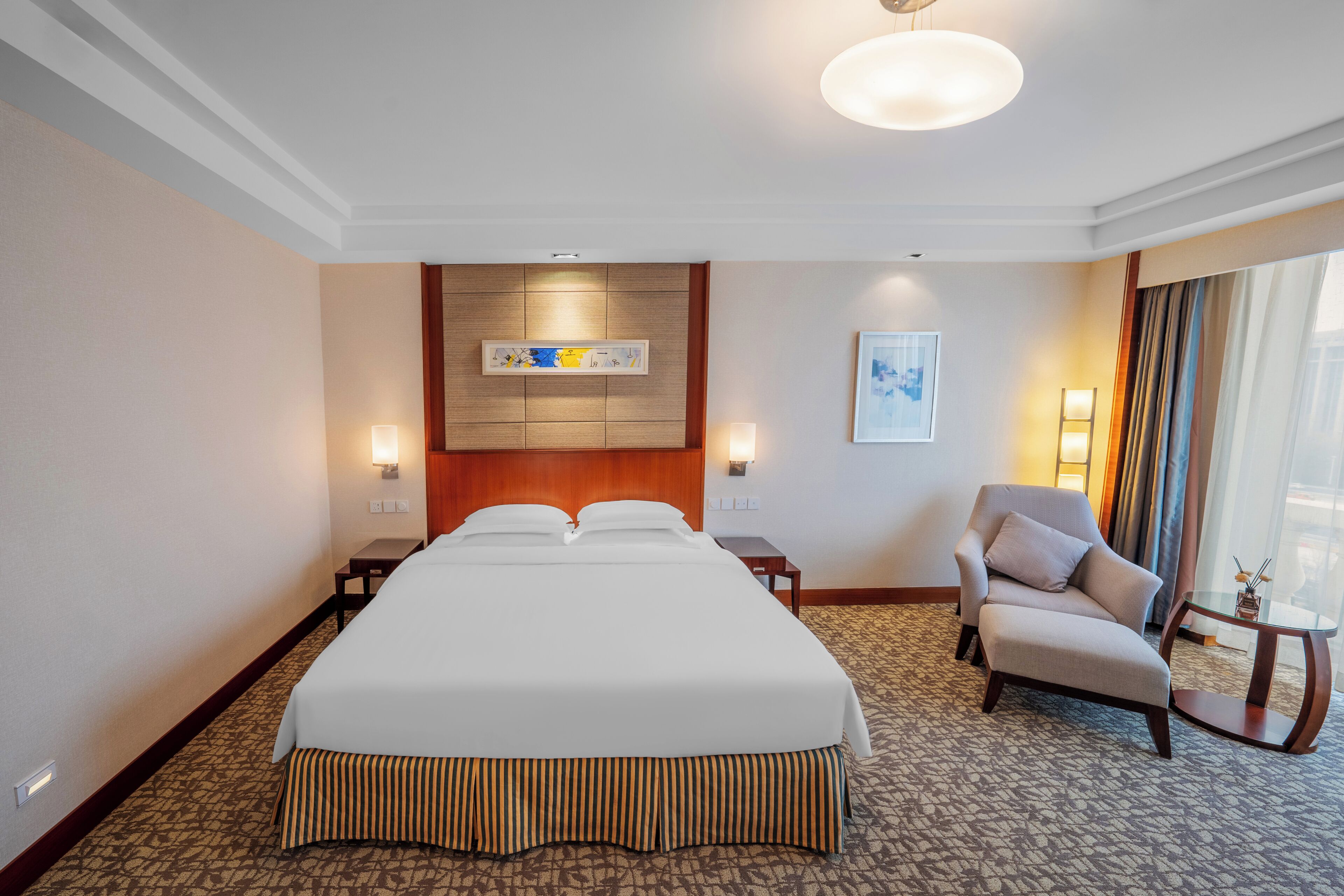 Habitación de hotel con una cama grande, una silla, una mesita y un cuadro en la pared.