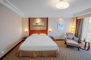 Habitación de hotel con una cama grande, una silla, una mesita y un cuadro en la pared.