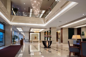 A spacious lobby with a high ceiling, a chandelier, a reception desk, and a seating area. - Beijing Meida Hotel (Changping)