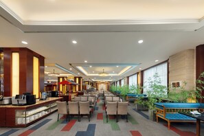 A hotel lobby with a reception desk, seating area, and large windows.