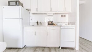 A modern kitchen with white cabinetry, a built-in microwave, a stove, and a sink. - Cute Studio in the center of Waikīkī with Parking (Honolulu)
