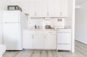 A modern kitchen with white cabinetry, a built-in microwave, a stove, and a sink. - Cute Studio in the center of Waikīkī with Parking (Honolulu)
