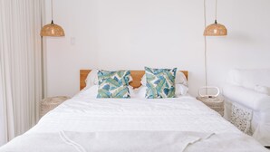 A neatly made bed with white bedding, two decorative pillows with a leaf pattern, and a bedside table with a woven basket. - Cute Studio in the center of Waikīkī with Parking (Honolulu)