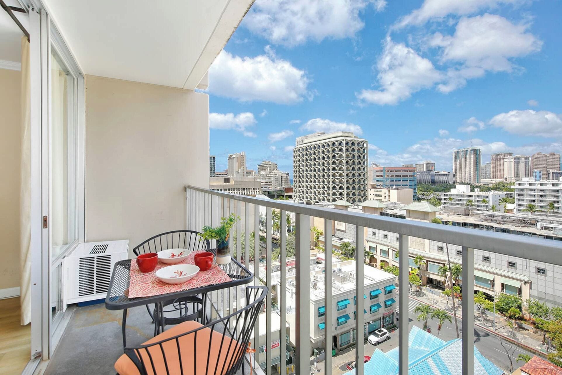 A balcony with a table set for two, a chair, and a view of the cityscape.