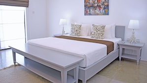 A modern bedroom with a large bed, two bedside tables with lamps, a painting on the wall, and a view through the window.