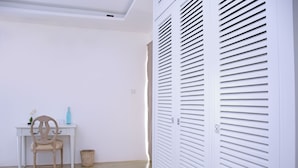A room with a white desk, a chair, a wicker basket, and a white closet with horizontal slats.