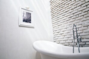 Ein Badezimmer mit einer weißen Badewanne, einer weißen Wand und einer Ziegelwand.