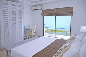 Ein Schlafzimmer mit Bett, Schreibtisch und Stuhl, ein großes Fenster mit Meerblick und einem Kleiderschrank.