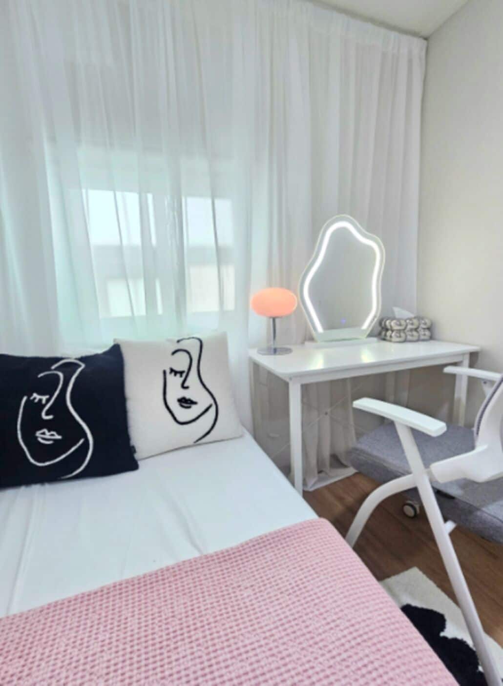 A hotel room with a bed, a desk, a chair, and a large window with sheer curtains.