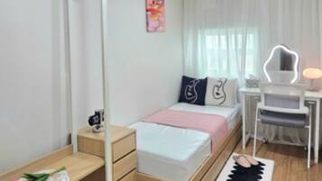 A modern bedroom with a bed, bedside table, desk, chair, and a mirror.