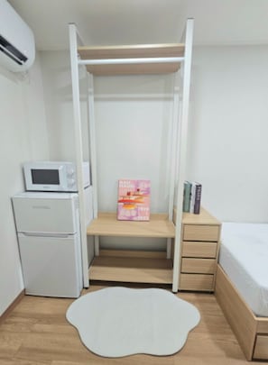 Ein kleines Zimmer mit einem Bett, einem Schreibtisch, einer Mikrowelle und einem Bücherregal.