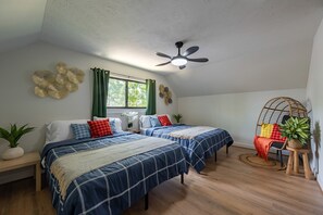 Ein Schlafzimmer mit zwei Betten, einem Deckenventilator, einem Fenster mit Vorhängen und einem kleinen Tisch mit Pflanze.