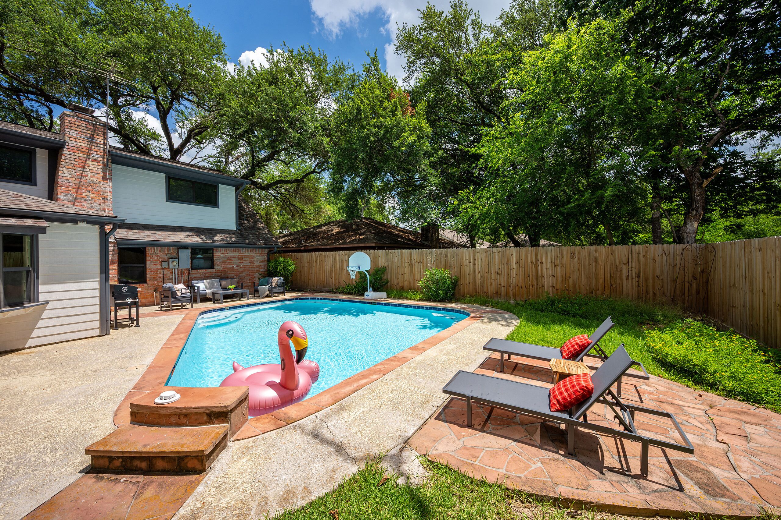 A backyard with a swimming pool, a flamingo float, and a wooden deck with lounge chairs.