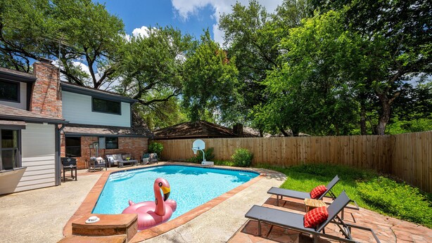 En have med swimmingpool, en flamingo-svømmebøje og en træterrasse med liggestole.