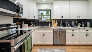 Et moderne køkken med rustfrie stålgrebe, hvide skabe og en backsplash med sorte fliser.