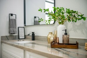 A bathroom vanity with a marble countertop, a white vase with green foliage, and various toiletries.