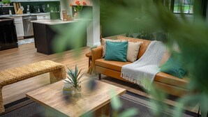En moderne stue med sofa, sofabord og spiseplads med et køkken i baggrunden.