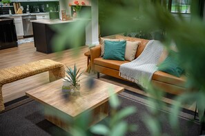 Ein modernes Wohnzimmer mit Sofa, Couchtisch und Essbereich, im Hintergrund eine Küche.