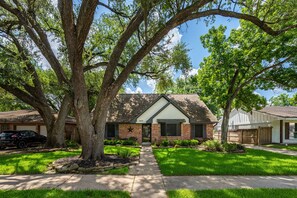 A residential house with a front yard, a driveway, and a large tree. - Cozy 5-bedroom house in adorable Spring with pool (Spring)