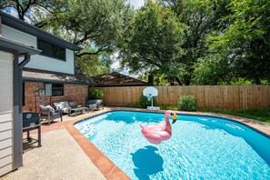 A backyard with a swimming pool, a wooden fence, and a flamingo float.