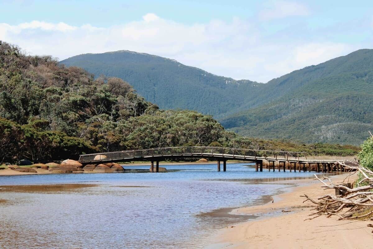 A wooden bridge over a river with a forested hillside in the background.