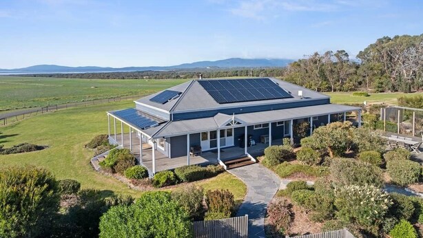 Ein modernes Haus mit überdachter Veranda, Solaranlage und Blick auf die Landschaft.