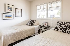 Quarto com duas camas, uma janela com vista e três quadros na parede.