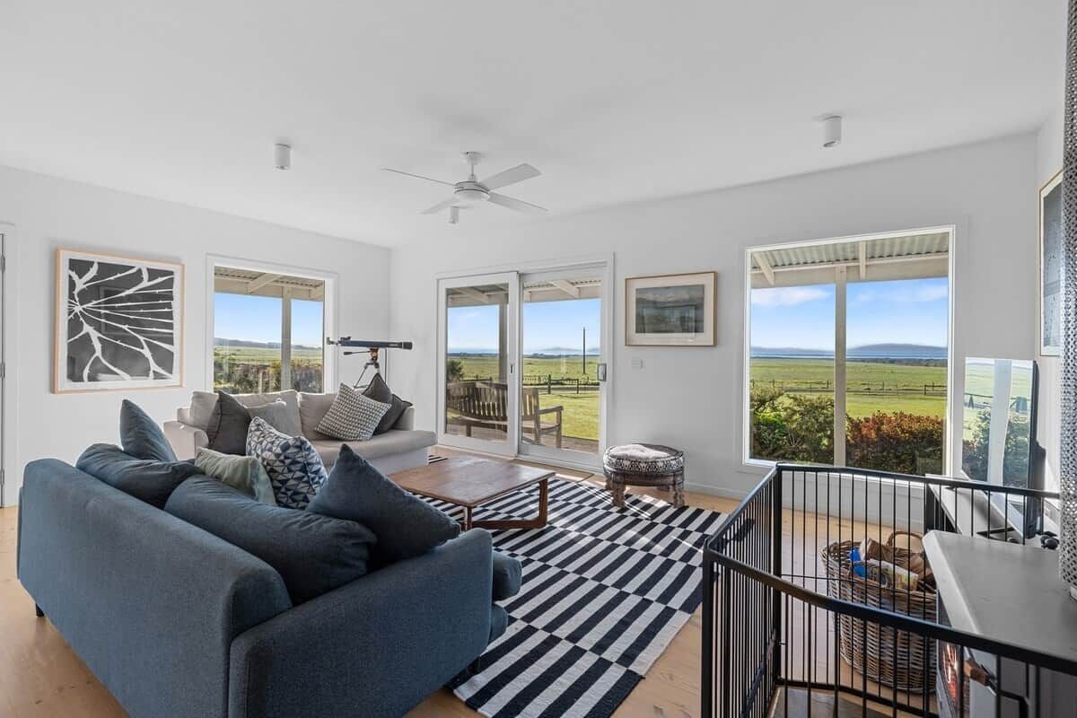A spacious living room with a sofa, a coffee table, and a view of the outdoors through large windows.