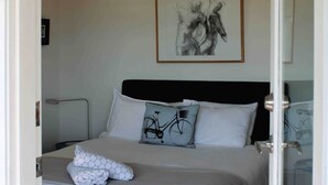 Ein Schlafzimmer mit einem Bett, Kissen, einem gerahmten Kunstwerk an der Wand und einer Tür zu einem anderen Raum.