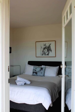 A bedroom with a bed, pillows, a framed artwork on the wall, and a door leading to another room. - The Yanakie House - Wilsons Promontory (Yanakie)
