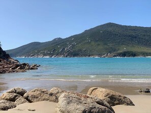 A beach with large rocks in the foreground, a clear blue sea, and a hill with vegetation in the background. - The Yanakie House - Wilsons Promontory (Yanakie)