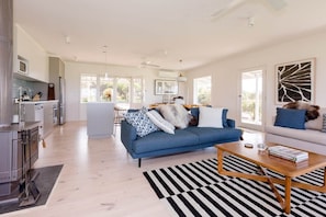 A modern living room with a sofa, coffee table, and a kitchen area with appliances. - The Yanakie House - Wilsons Promontory (Yanakie)