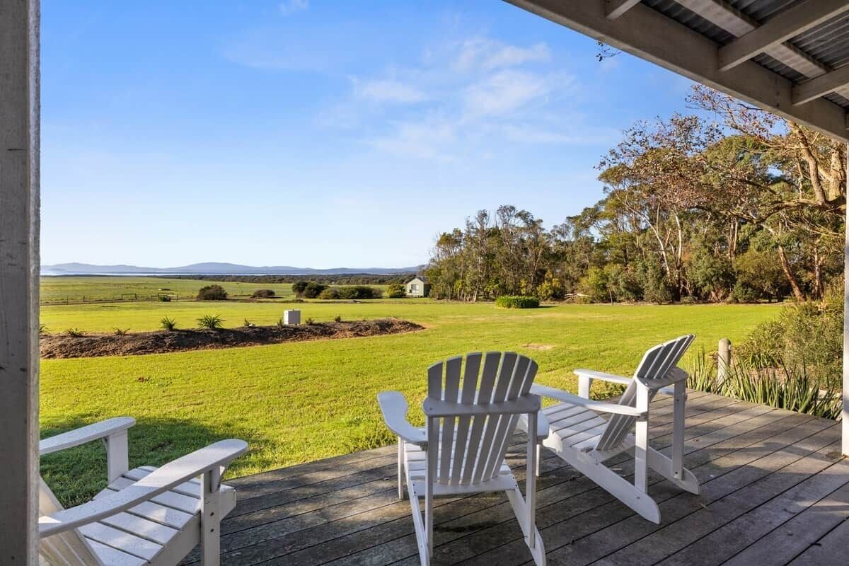 A covered outdoor area with two Adirondack chairs facing a grassy field and distant hills.