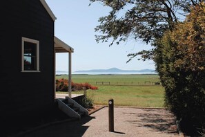 A building with a porch and a view of a green field and mountains. - Wattle - The Yanakie House - Wilsons Promontory (Yanakie)
