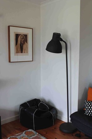 Ein Raum mit einer schwarzen Stehlampe, einem gerahmten Bild an der Wand, einem schwarzen Sitzsack und einem gemusterten Teppich.