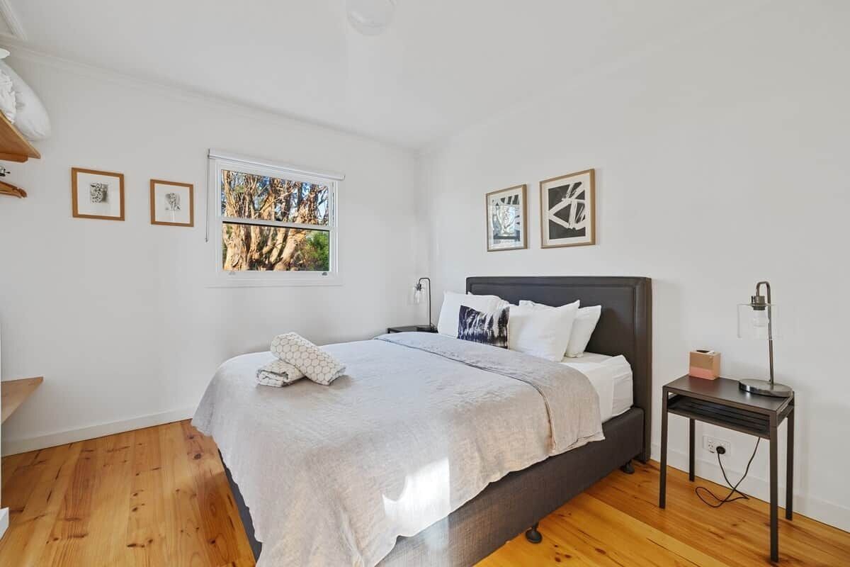 Une chambre à coucher avec un lit, une table de chevet, une fenêtre et des œuvres d’art murales.