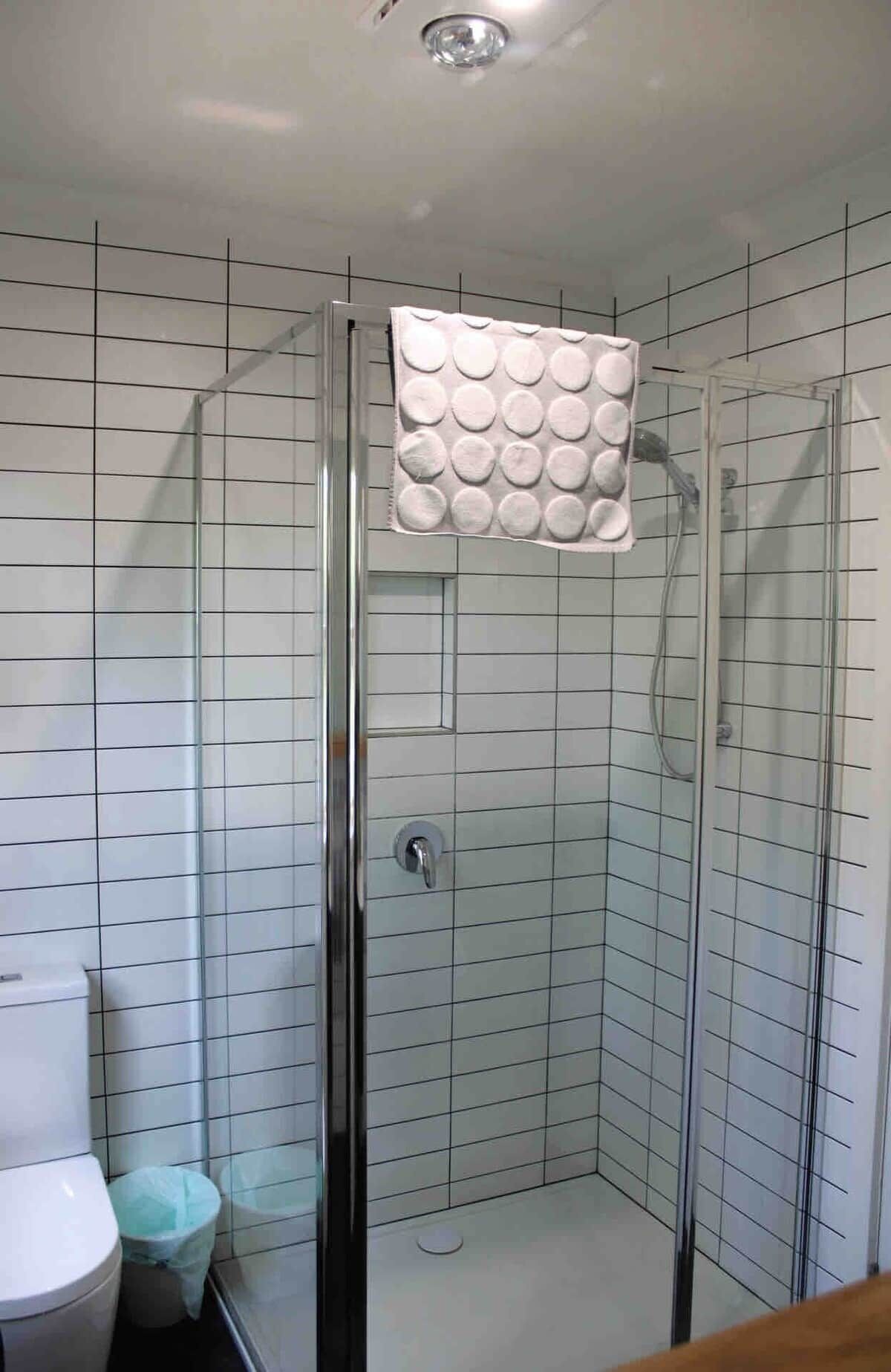A shower with a glass door, a white tiled wall, and a visible showerhead.