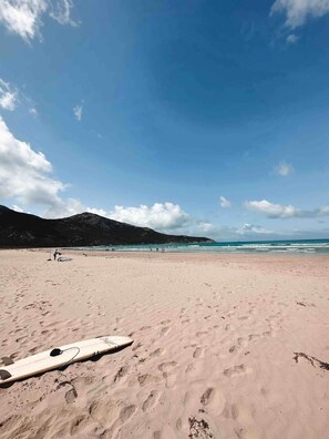 Ein Strand mit einem Surfbrett, Fußspuren und einem Berg im Hintergrund.