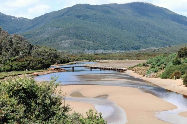 Un fiume con un ponte di legno, circondato da dolci colline e vegetazione rada.