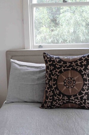 A bed with a grey pillow and a patterned pillow.