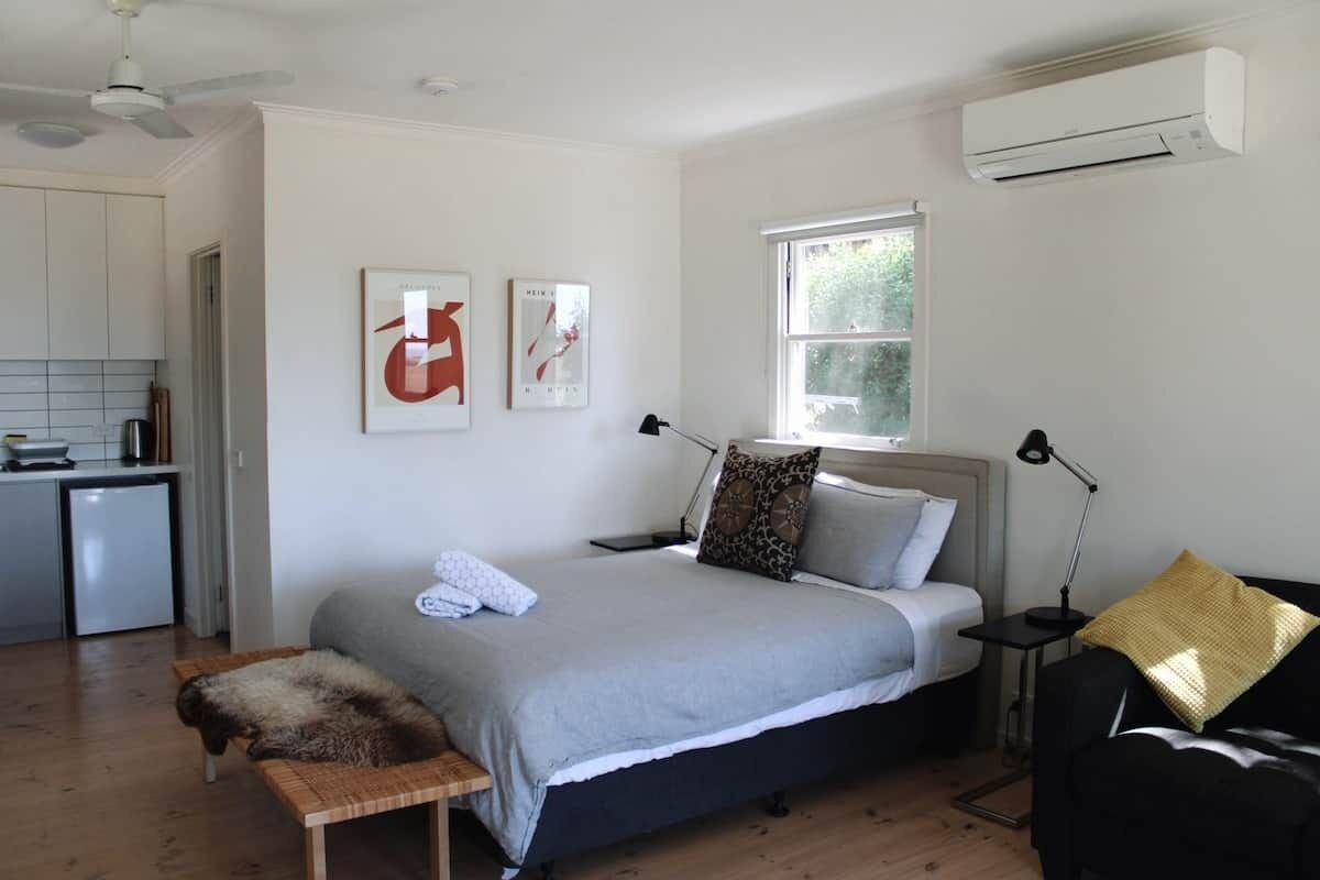 A bedroom with a bed, a bedside table, a lamp, a window, and a wall-mounted air conditioner.