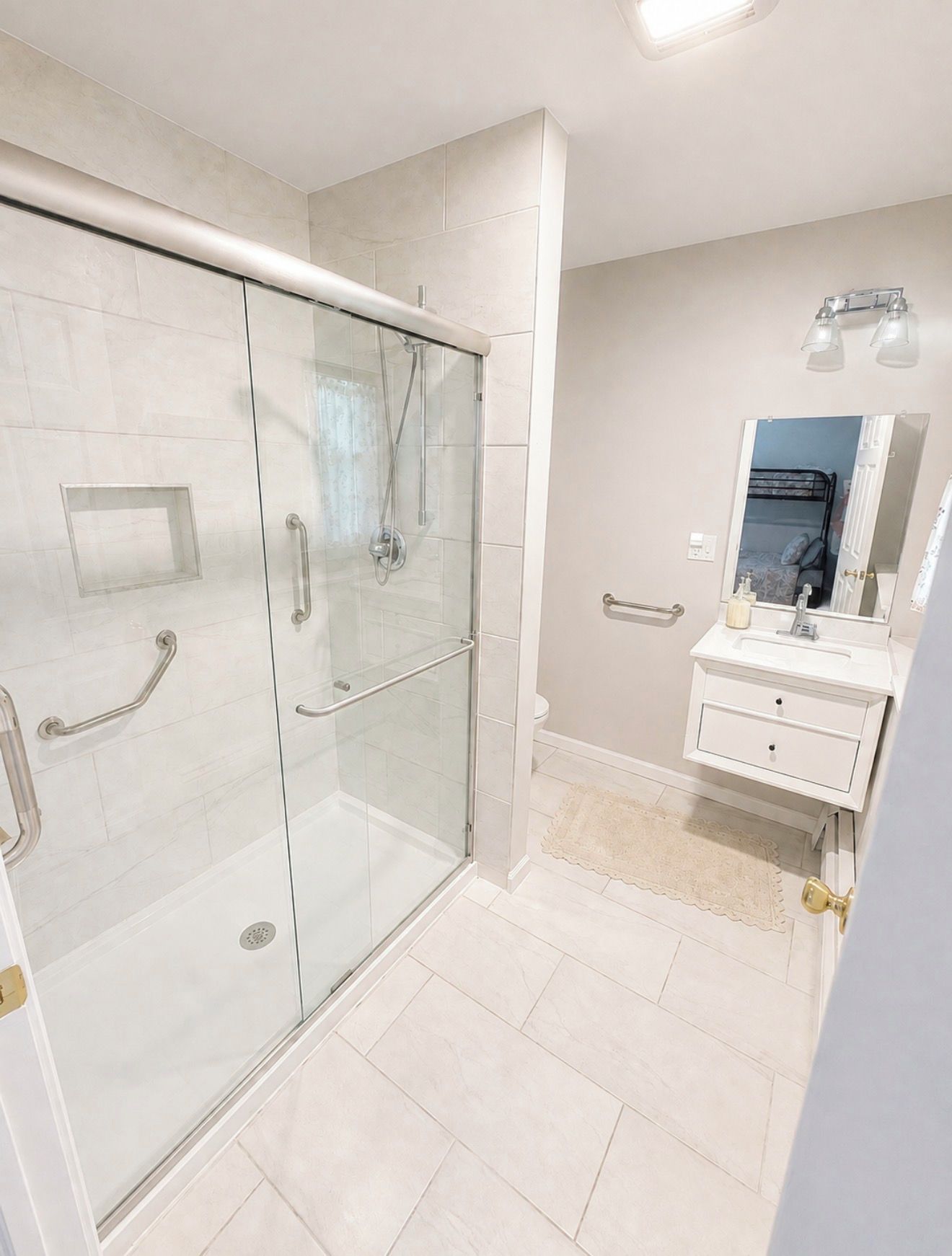 A modern bathroom with a glass-enclosed shower, a white vanity with a mirror, and a beige tiled floor.