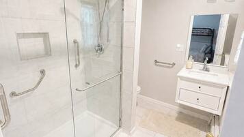 A modern bathroom with a glass-enclosed shower, a white vanity with a mirror, and a beige tiled floor.
