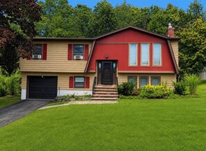 A two-story house with a red front, beige siding, and a black garage door. - Spacious 4BR/2BT Hiking trails, Lake, Legoland & Warwick (Monroe)