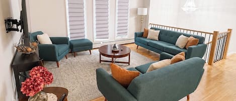 A spacious living room with a sofa set, a coffee table, and a TV mounted on the wall.