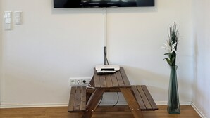 Ein Flachbildfernseher ist an einer Wand über einem Holztisch angebracht, auf dem sich eine Blumenvase befindet.