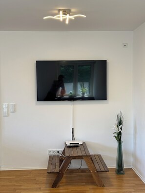A flat-screen TV mounted on a wall above a wooden table with a vase of flowers. - Bergblick Buchenhöhe: modern vacation rental at 1,000 m, surrounded by forest. (Berchtesgaden)