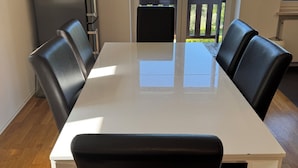Ein Essbereich mit weißem Tisch und schwarzen Stühlen, einem schwarzen Kühlschrank sowie Blick auf einen Balkon mit Holzgeländer.